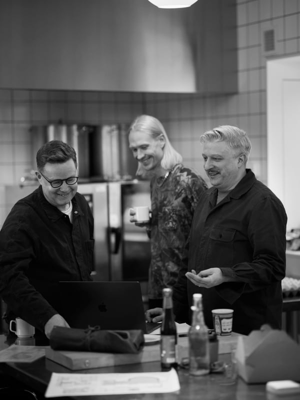 Black and white photo of three people in conversation in a kitchen.